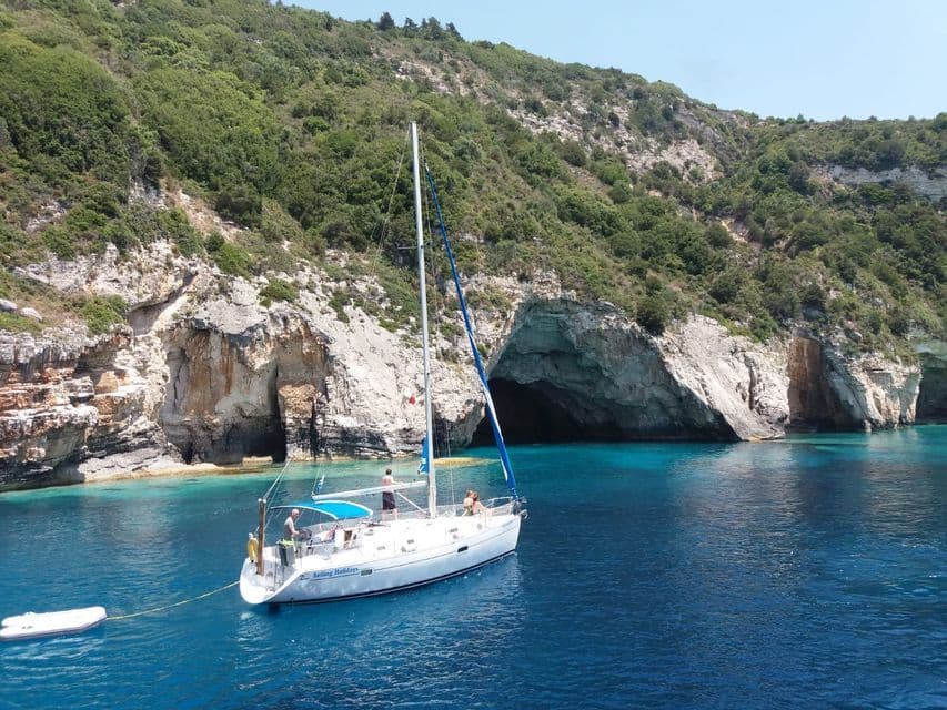 Eine WeRoad Gruppenreise auf einem Segelboot, das in einer türkisen Bucht neben einer felsigen Klippe mit Meereshöhlen ankert.