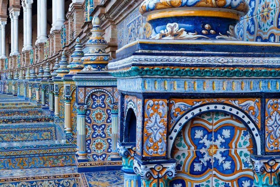 An ornate balustrade decorated with colorful blue and orange ceramic tiles recedes into the distance next to a colonnade.