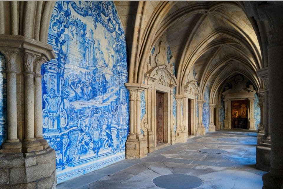 An arched stone hallway with a vaulted ceiling, decorated with a large mural of blue and white tiles.