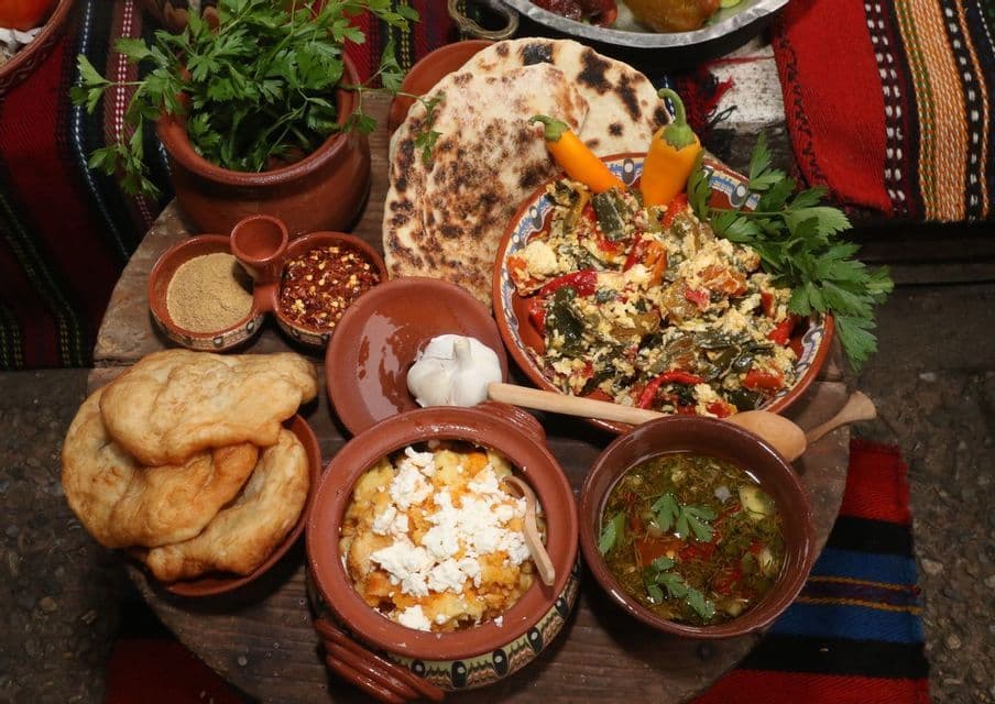 A traditional meal spread on a wooden surface, featuring various dishes in earthenware bowls, flatbread, and spices.