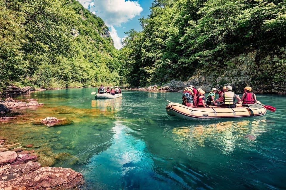 Rafting di gruppo WeRoad su due gommoni in un fiume turchese che attraversa un canyon lussureggiante.