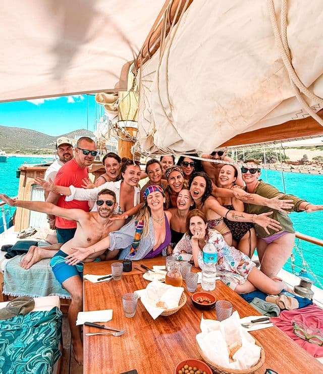 Un grande gruppo WeRoad in viaggio posa e sorride per una foto sul ponte di legno di una barca, con acqua turchese sullo sfondo.