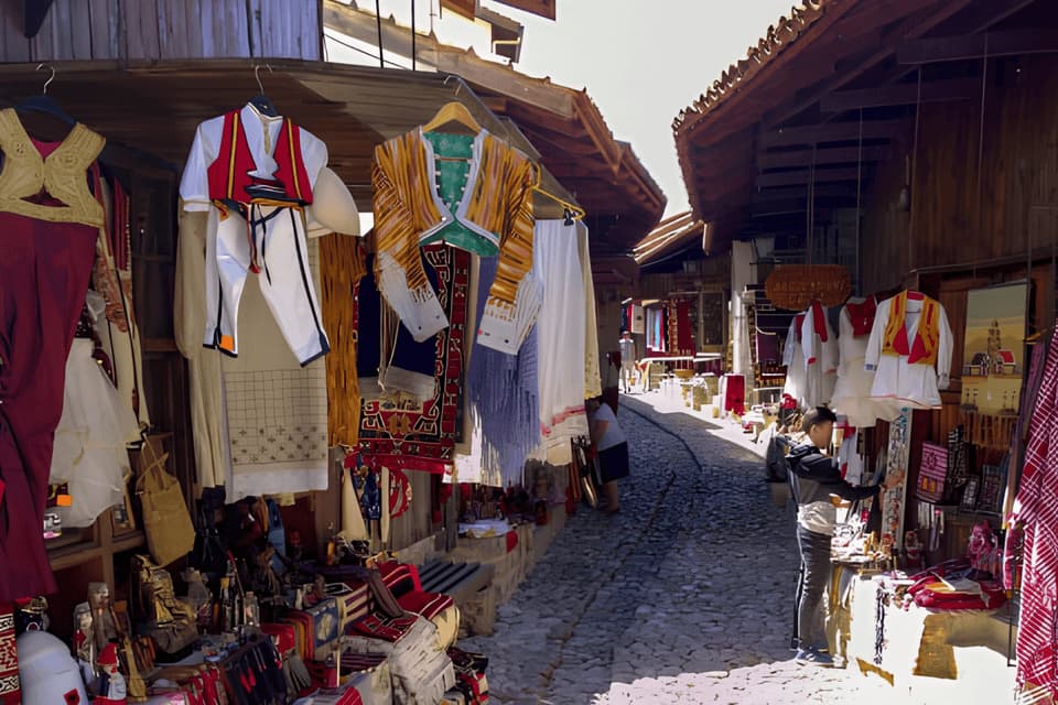 Abbigliamento tradizionale e souvenir in vendita in un mercato all'aperto lungo una stretta strada acciottolata.