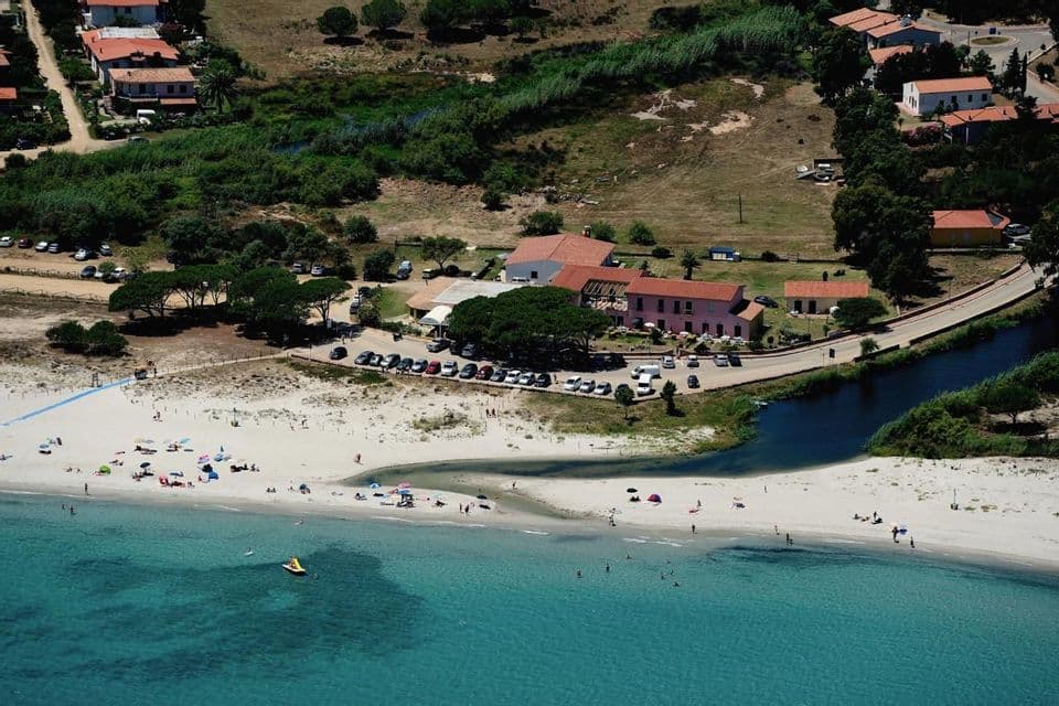 Veduta aerea di una spiaggia di sabbia bianca con persone che si godono l'acqua turchese, dove un estuario fluviale incontra il mare vicino a una città costiera.