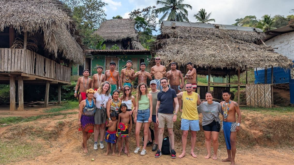Un groupe WeRoad en voyage pose pour une photo avec des membres d'une communauté autochtone dans un village aux huttes de chaume.