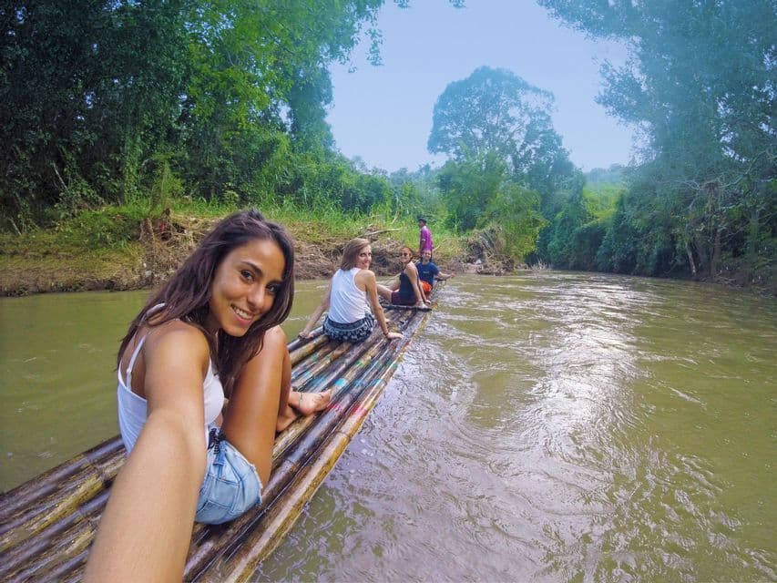 Une femme se prend en selfie, souriante, avec son groupe WeRoad, sur un radeau en bambou flottant sur une rivière au cœur de la jungle.