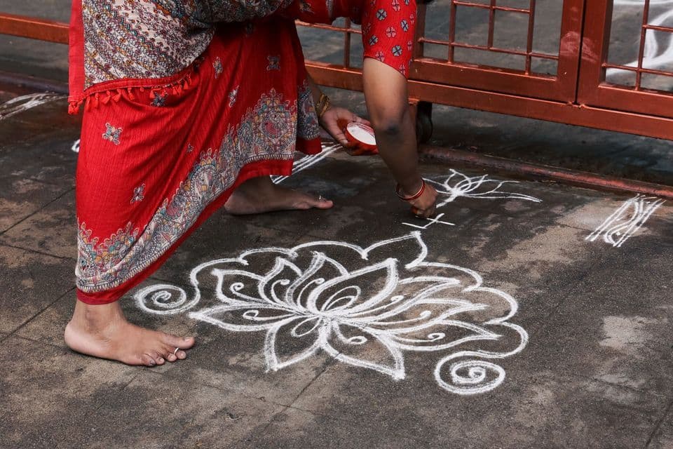 Una mujer con un sari rojo estampado dibuja un gran diseño floral blanco en el pavimento con polvo.