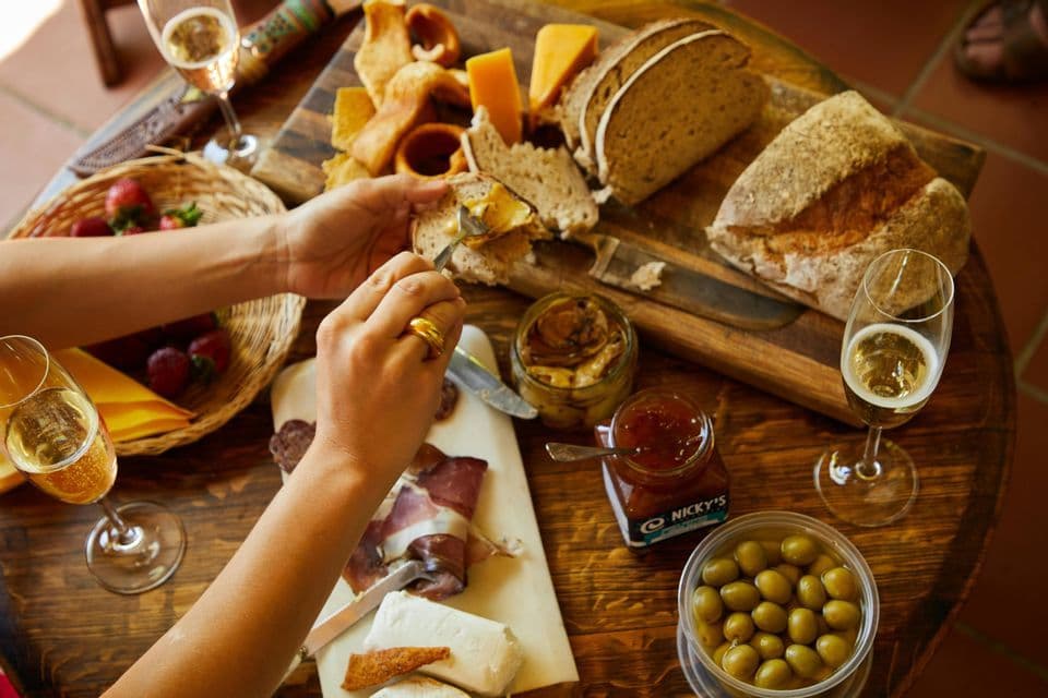A top-down view of a charcuterie board with bread, cheese, olives, and glasses of sparkling wine on a wooden table.