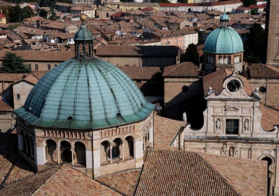 Una veduta dall'alto dei tetti in terracotta di una città storica, con due prominenti cupole in verderame su antichi edifici.