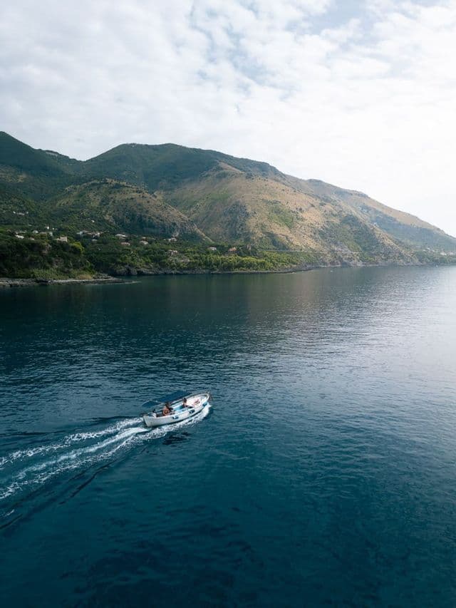 Vista aerea di un viaggio di gruppo WeRoad su una piccola barca che sfreccia sull'acqua vicino a una costa montuosa.