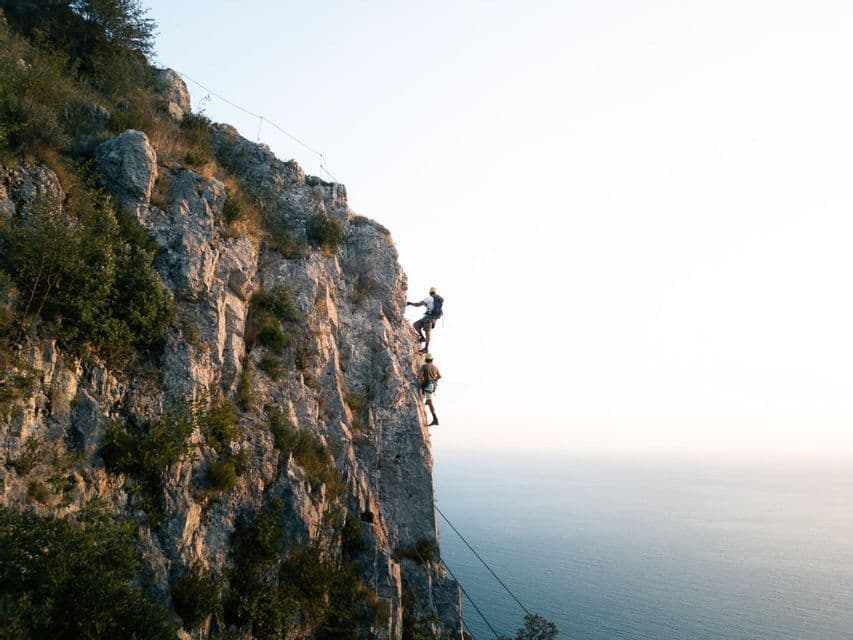 Due persone di un gruppo WeRoad fanno arrampicata su roccia su una ripida scogliera a picco sull'oceano.