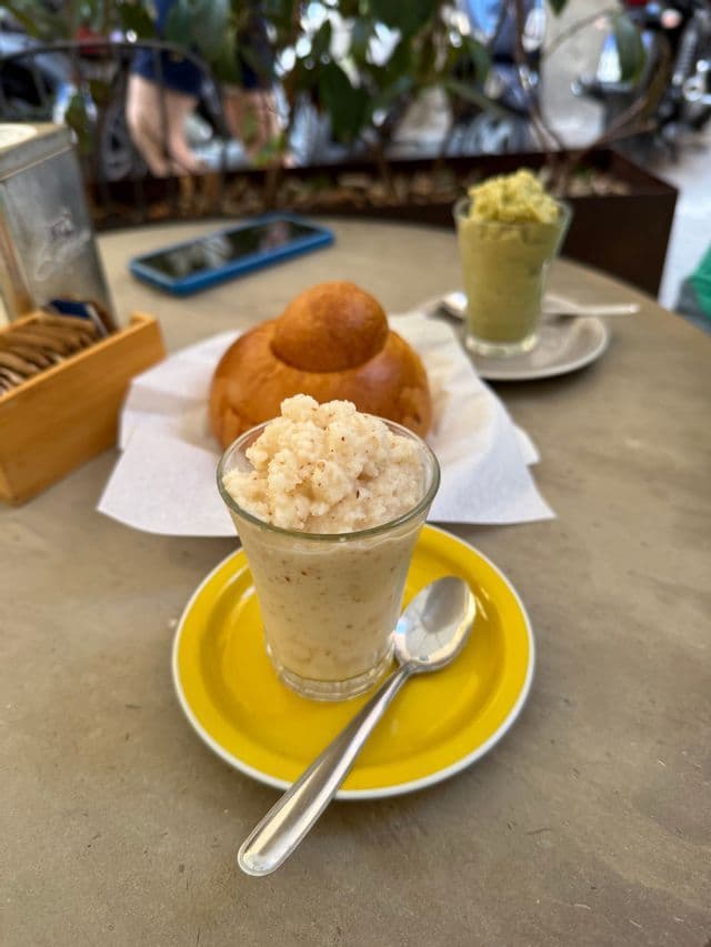Un bicchiere di granita su un piattino giallo con un cucchiaino, poggiato su un tavolo da caffè accanto a una brioche.