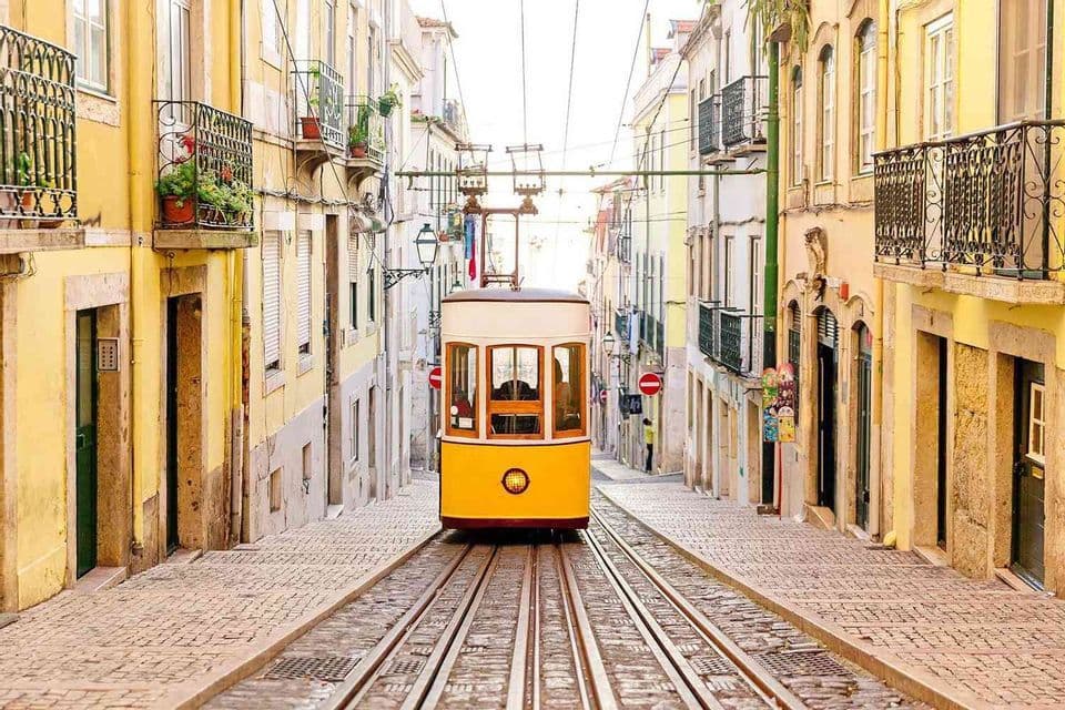 A yellow tram on tracks runs up a steep, narrow cobblestone street between tall, colorful buildings.