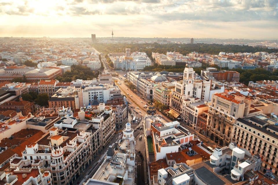 Aerial view of a sprawling city with a wide avenue cutting through historic buildings during a golden sunset.