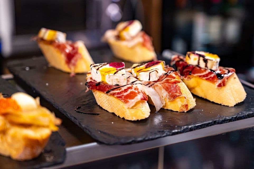 Spanish pintxos on a slate platter, topped with cured ham, cheese, and drizzled with balsamic glaze.