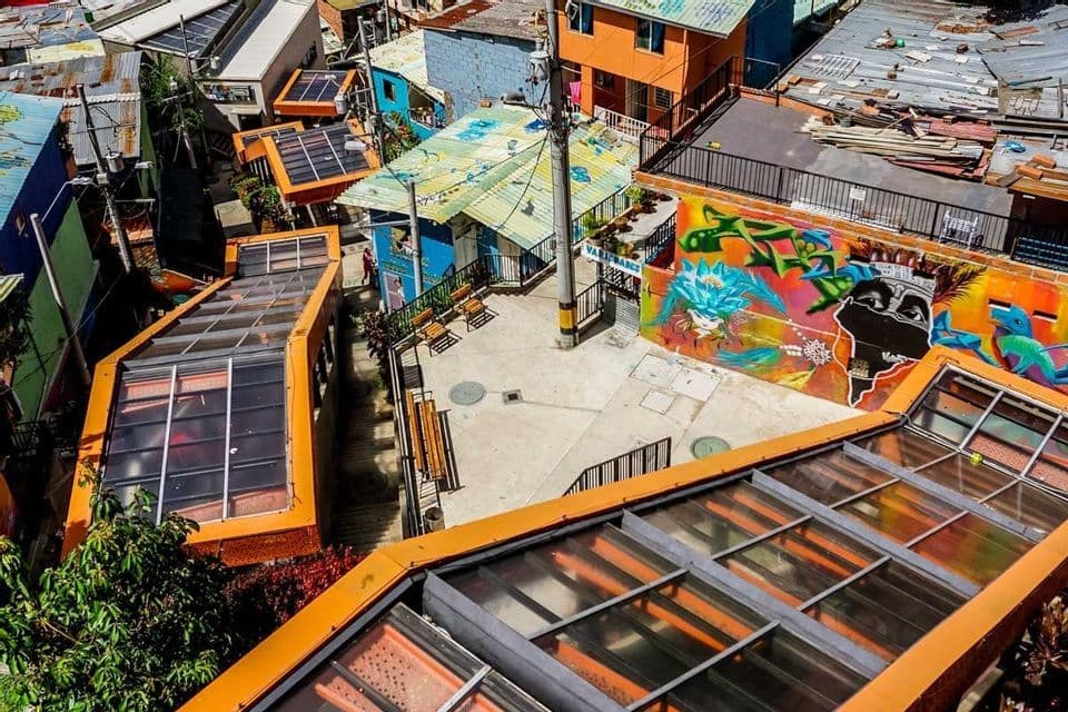 A high-angle view of orange-covered escalators ascending a colorful hillside neighborhood with graffiti on the walls.