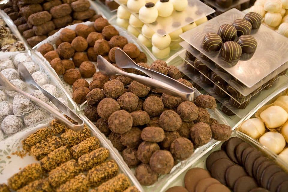 An assortment of chocolate truffles and candies arranged in serving trays with tongs ready to be served.