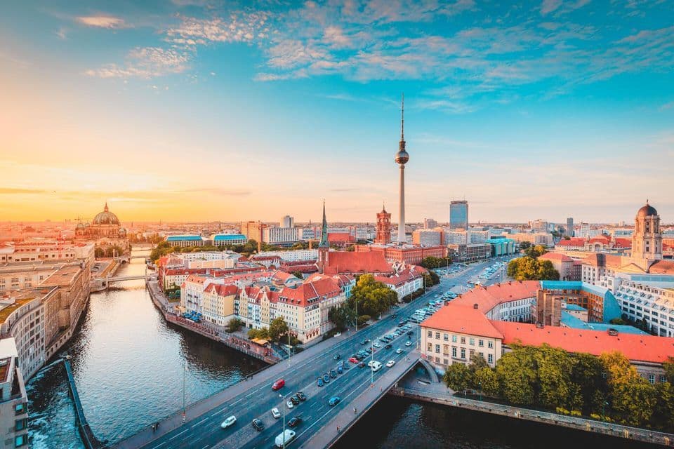 An aerial view of a cityscape with a prominent television tower and a domed building next to a river at sunset.