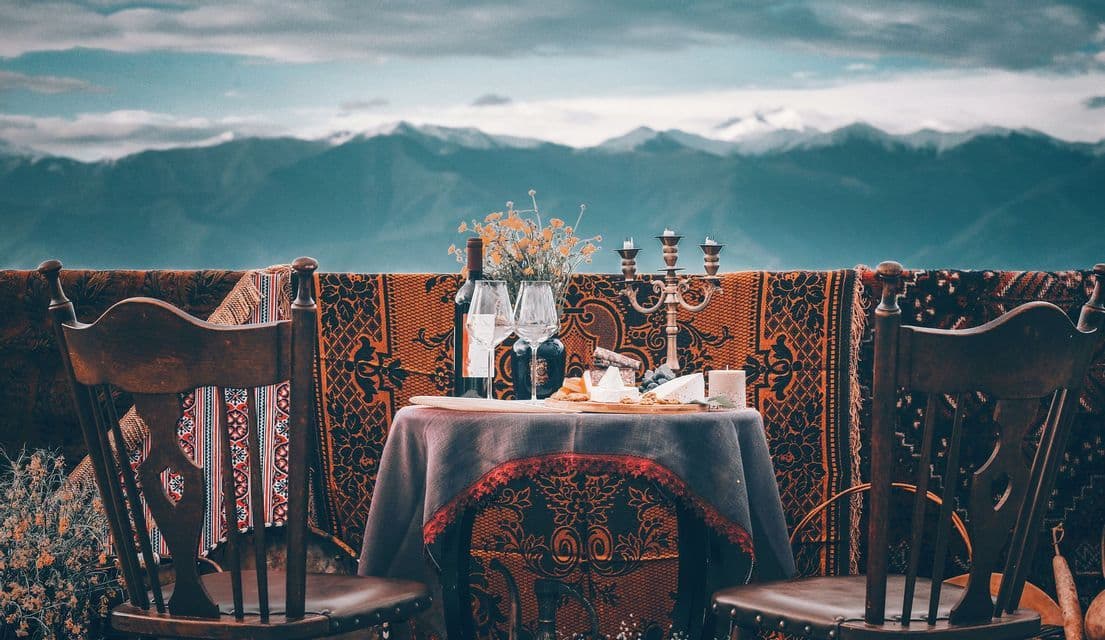 Una mesa para dos con vino y queso, con vistas a una vasta cordillera bajo un cielo nublado.