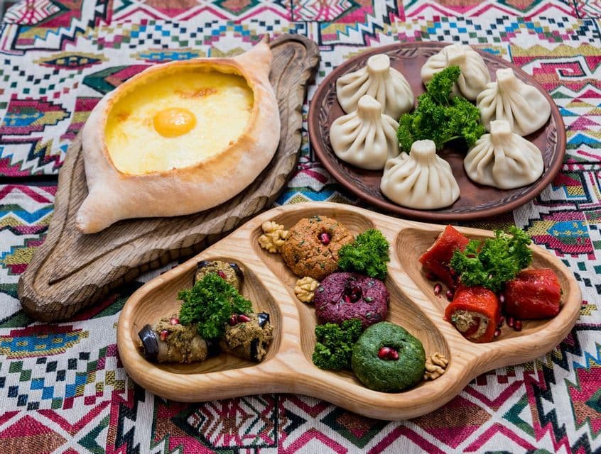Una mesa llena de platos tradicionales georgianos, como khachapuri con huevo, dumplings khinkali y aperitivos.