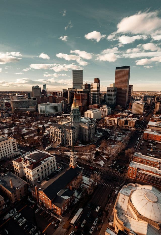 An aerial view of a city with a golden-domed capitol building and a modern skyline under a partly cloudy sky at golden hour.
