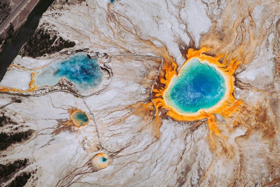 An aerial, top-down view of colorful geothermal hot springs, with a large blue and orange pool dominating the mineral-rich landscape.