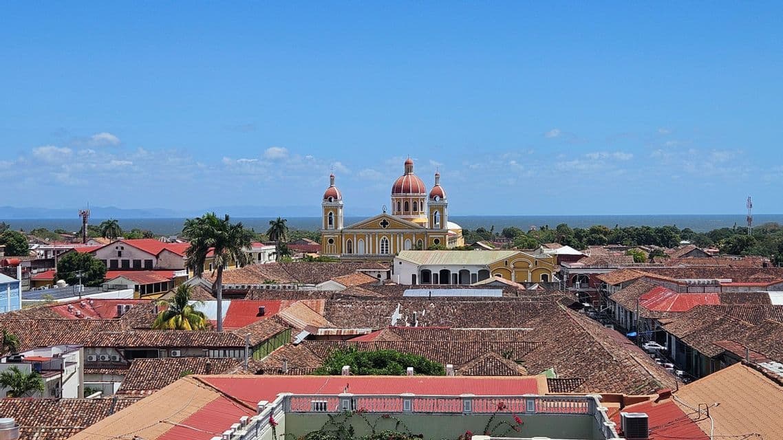 Ein Blick von oben auf eine Stadt mit Terrakotta-Dächern, einer zentralen gelben Kathedrale mit roten Kuppeln und dem Meer im Hintergrund.