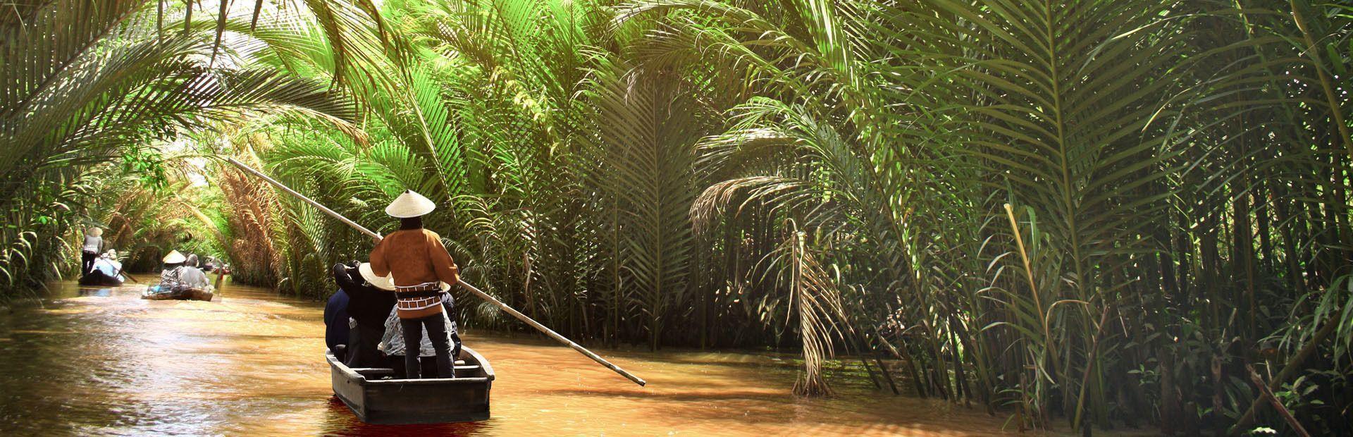 Eine WeRoad Gruppenreise fährt mit dem Boot auf einem engen Fluss, umgeben von dichten tropischen Palmen.