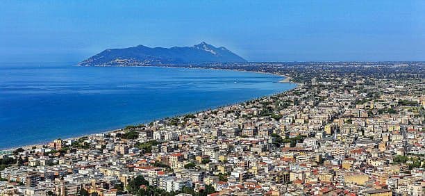 Una vista panoramica di una città costiera che si estende attorno a una baia, con una grande montagna visibile oltre l'acqua.