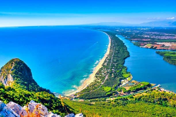 Una vista aerea di una lunga e stretta striscia di terra che separa l'oceano blu da un fiume calmo, con una montagna verde in primo piano.