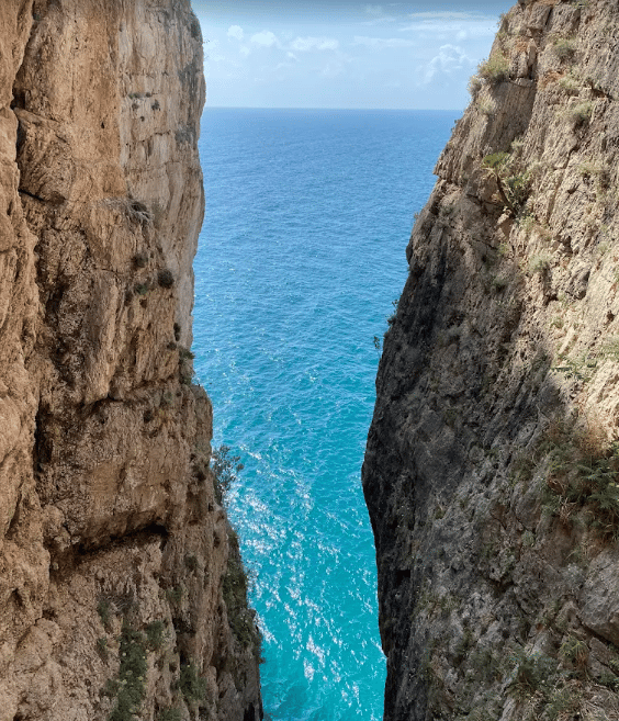 Una vista del mare azzurro tra due scogliere ripide e rocciose sotto un cielo sereno.