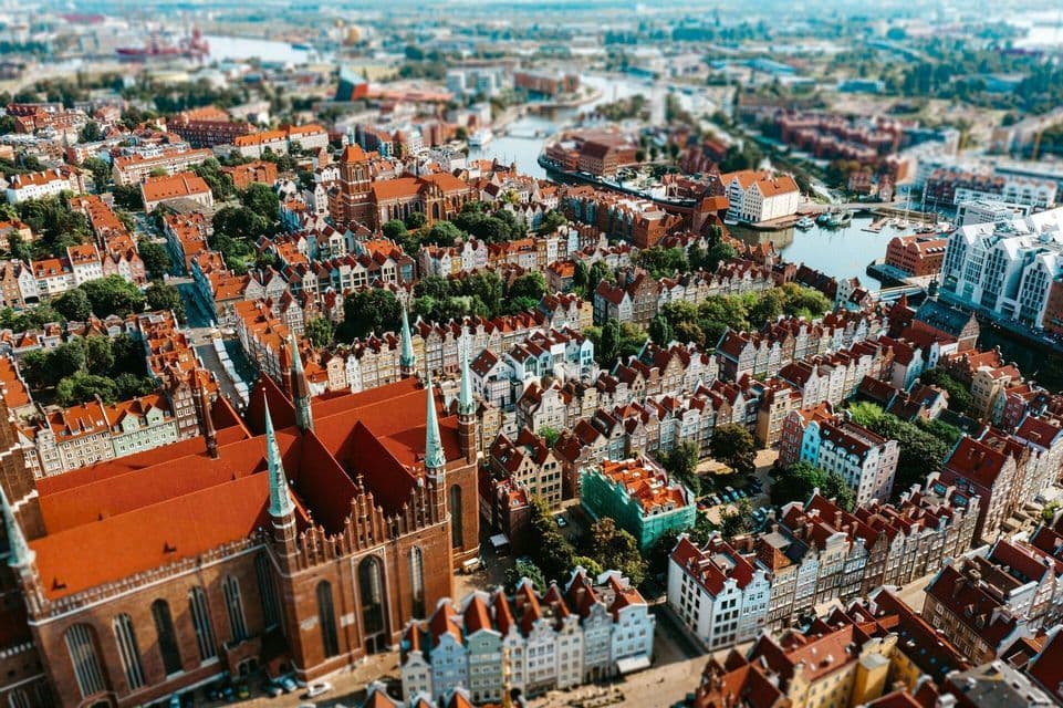 Vista aerea di una città storica con edifici dai tetti rossi e una grande cattedrale in mattoni, con effetto tilt-shift.