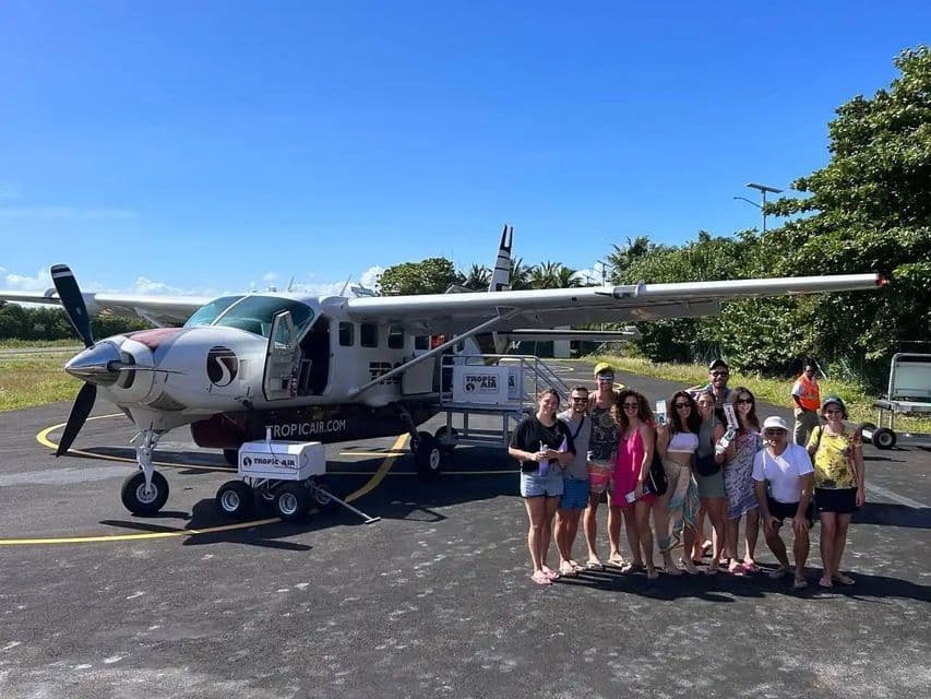A WeRoad group trip stands together for a picture on an airport tarmac in front of a small propeller plane.