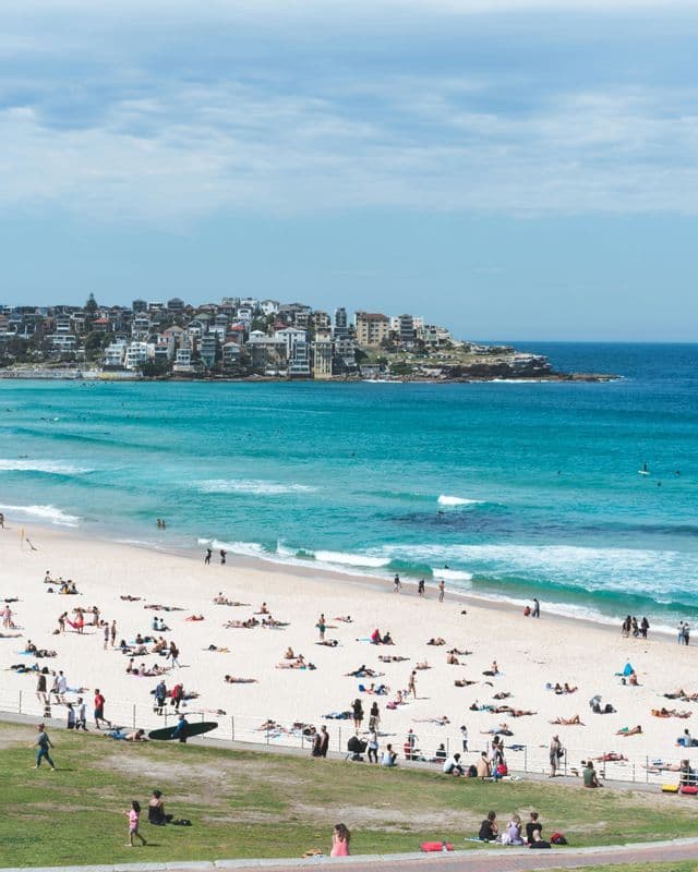 A high-angle view of a busy beach with people sunbathing on the sand and swimming in the turquoise water.