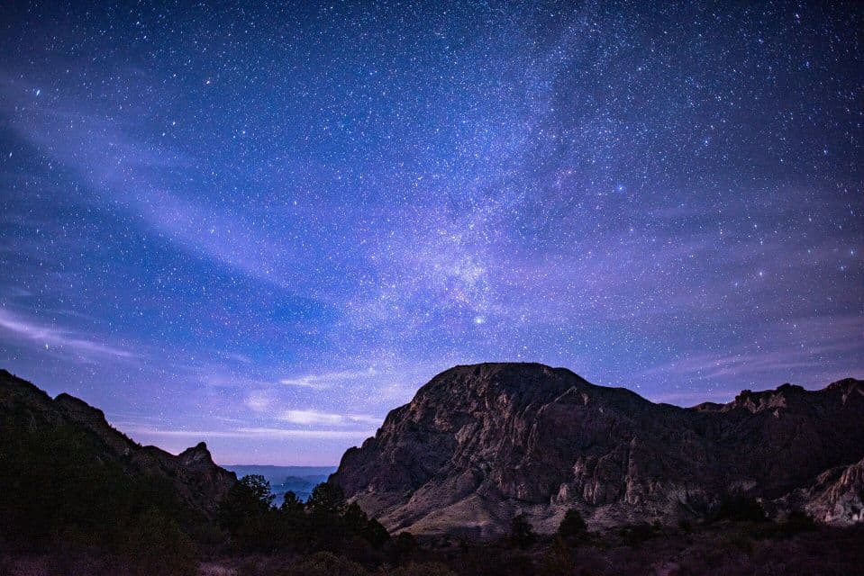 A vast starry night sky with the Milky Way galaxy visible above a silhouetted mountain range.
