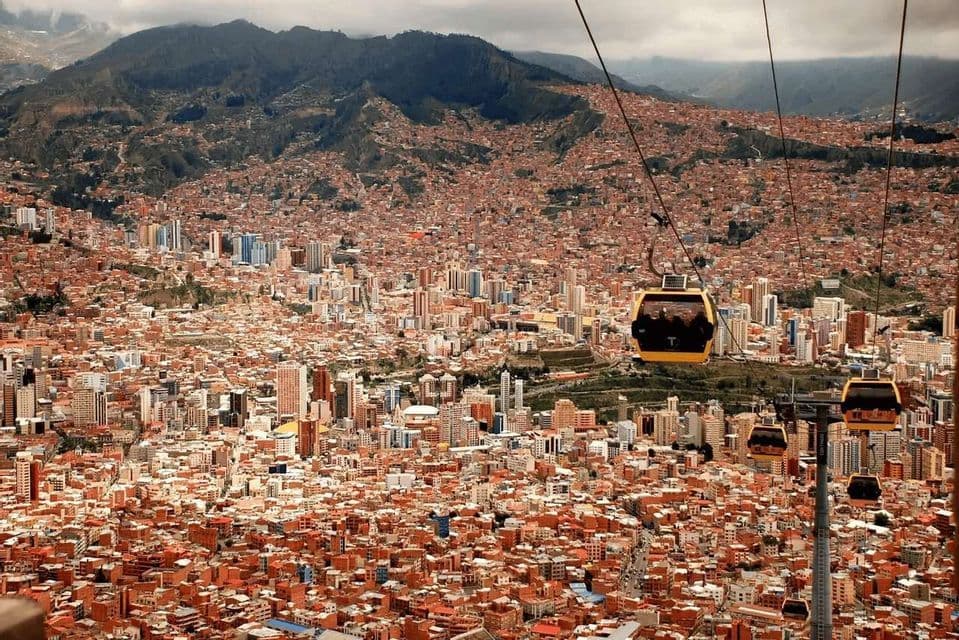 Teleféricos amarillos recorren una línea elevada sobre una densa ciudad de edificios con techos rojos, anidada junto a una cordillera.