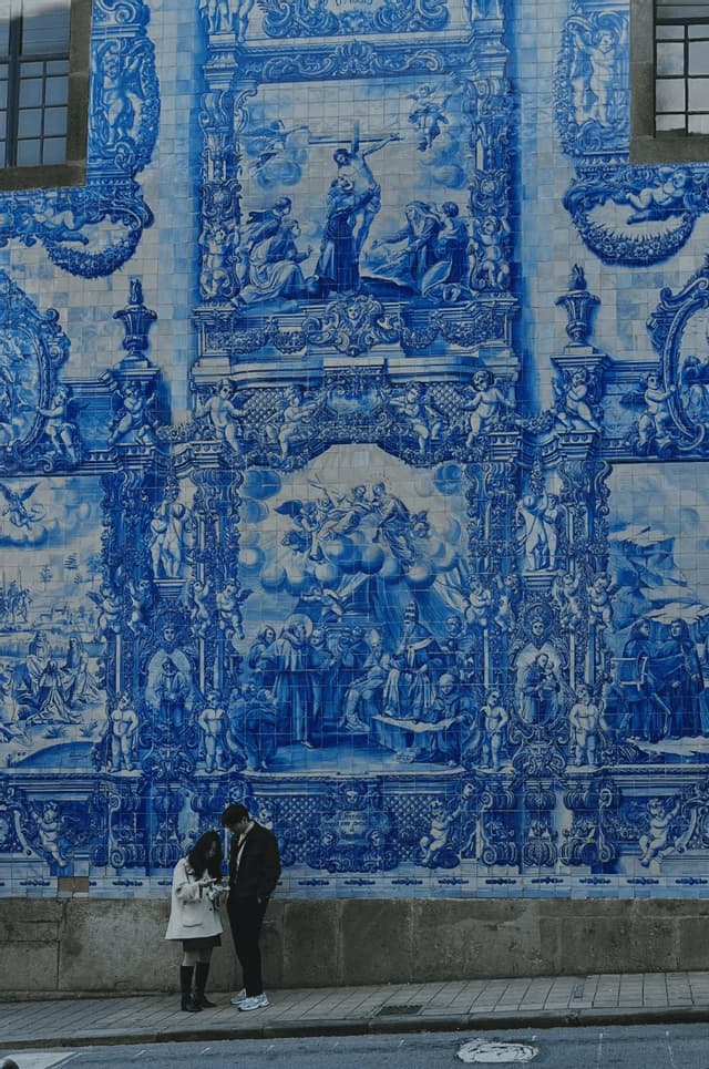 Un uomo e una donna stanno su un marciapiede davanti a un grande muro ricoperto di intricate piastrelle azulejo blu e bianche.