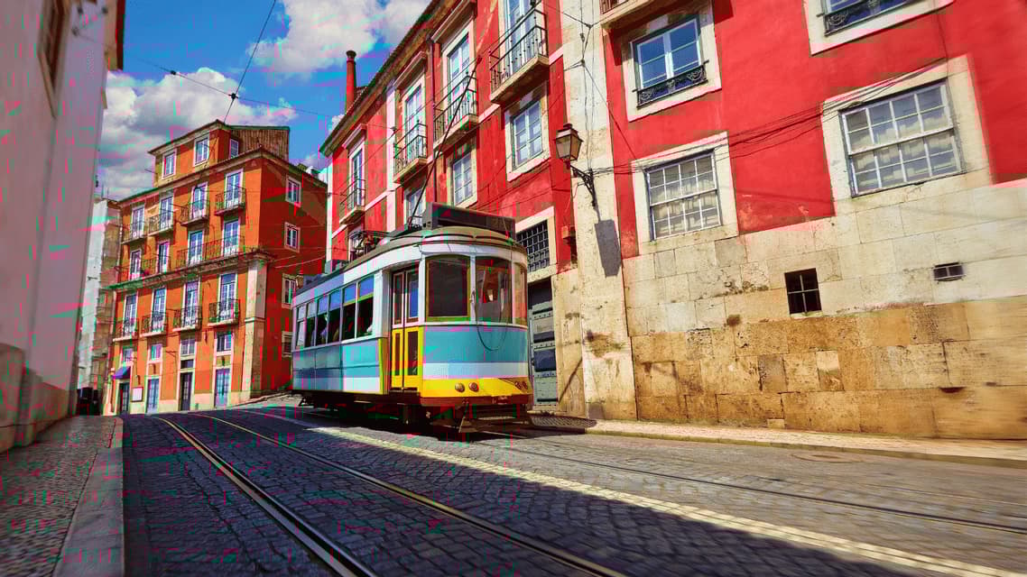 Un tram vintage colorato percorre i binari su una stretta strada acciottolata tra vivaci edifici rossi.