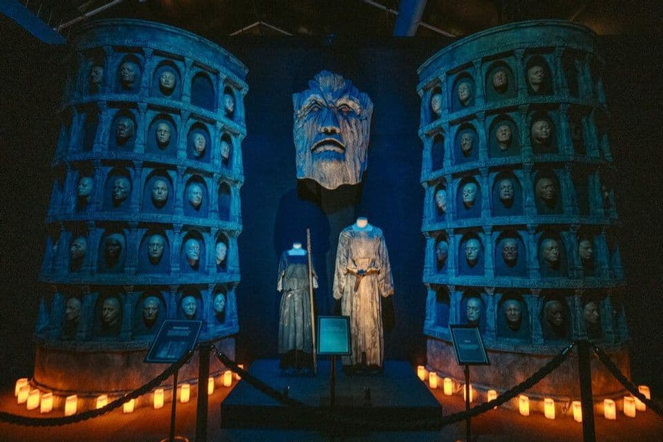 Un'esposizione buia con due alte colonne con volti in nicchie, che fiancheggiano due manichini in costume sotto una luce blu.