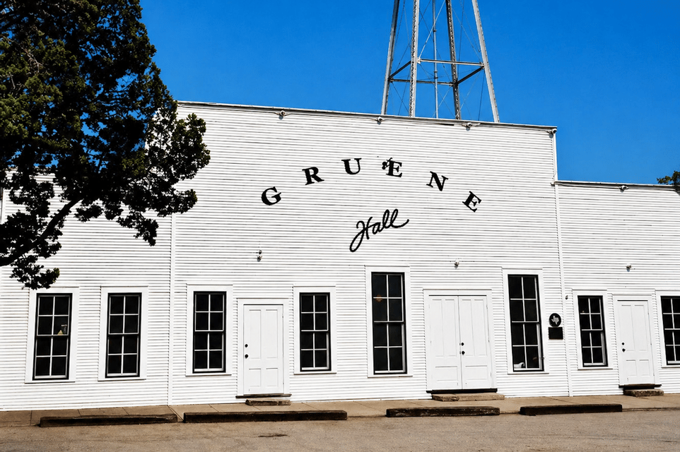 The white facade of the Gruene Hall building with its name in black letters, set against a clear blue sky with a water tower visible.