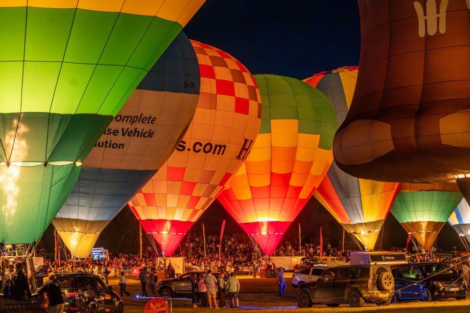Mongolfiere colorate illuminate dall'interno durante un festival notturno, con una folla che ammira da sotto.