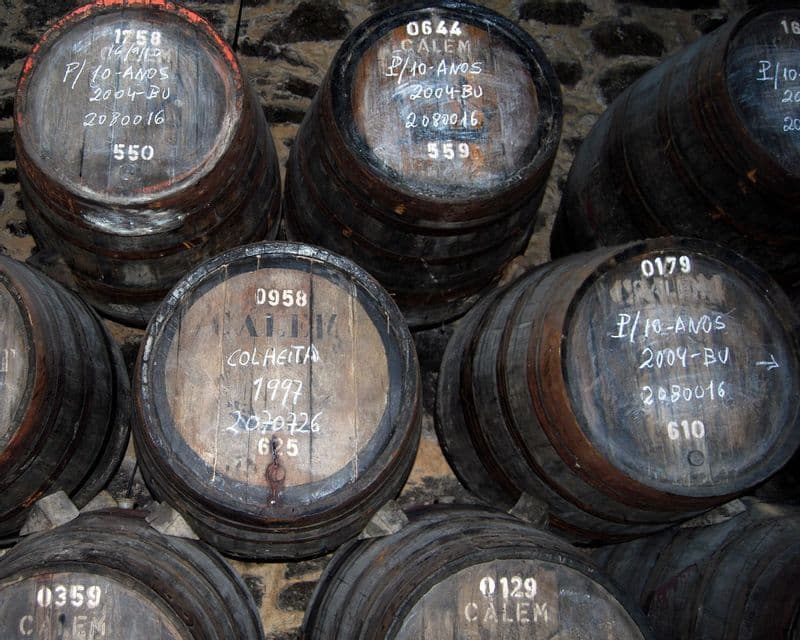 Numerose botti di legno di Porto Calem sono impilate in una cantina buia e con pareti in pietra, ciascuna contrassegnata con il gesso.