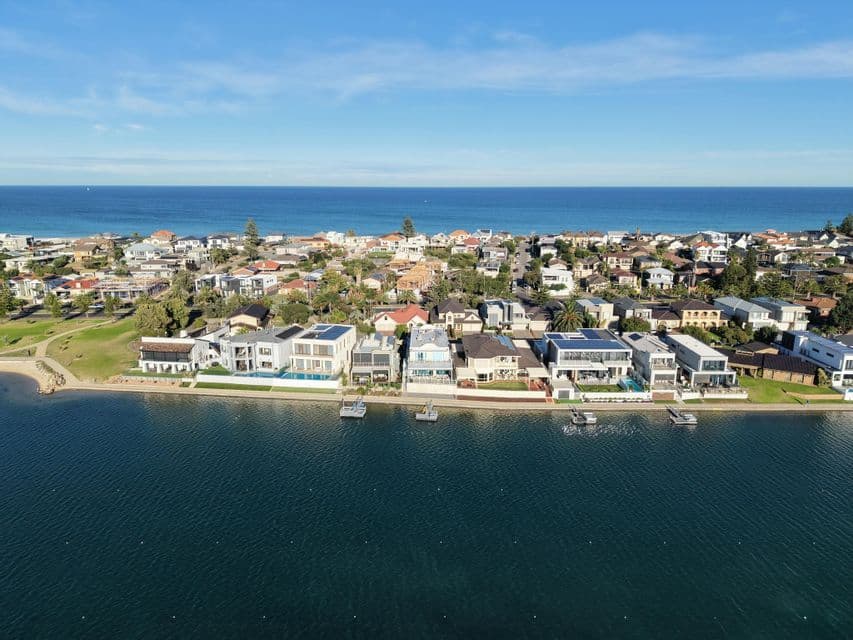 An aerial view of a coastal town nestled between a calm lake in the foreground and the wide ocean in the background.