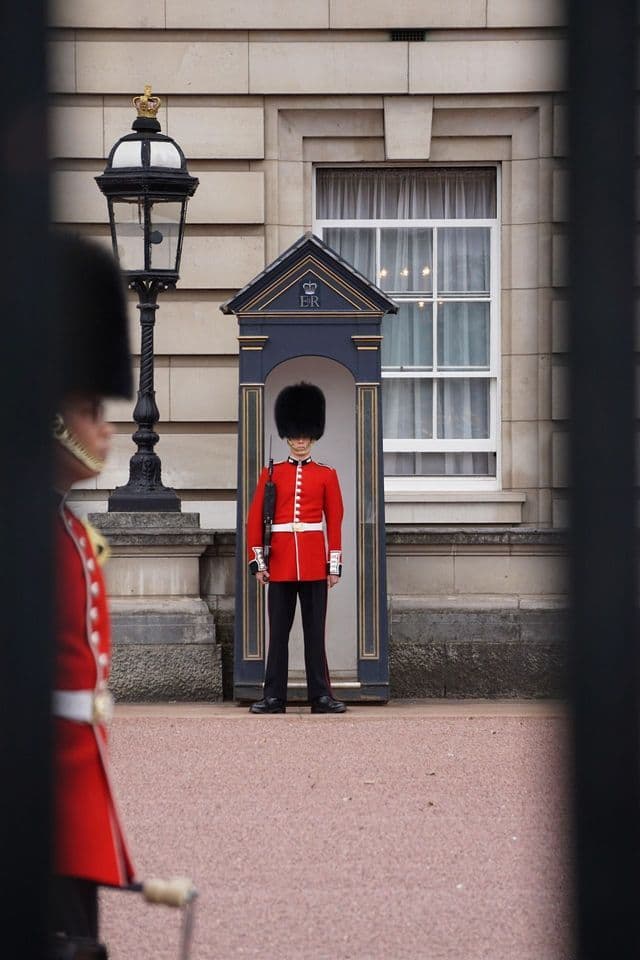 A Queen's Guard soldier in a red uniform and bearskin hat stands at attention inside a sentry box.