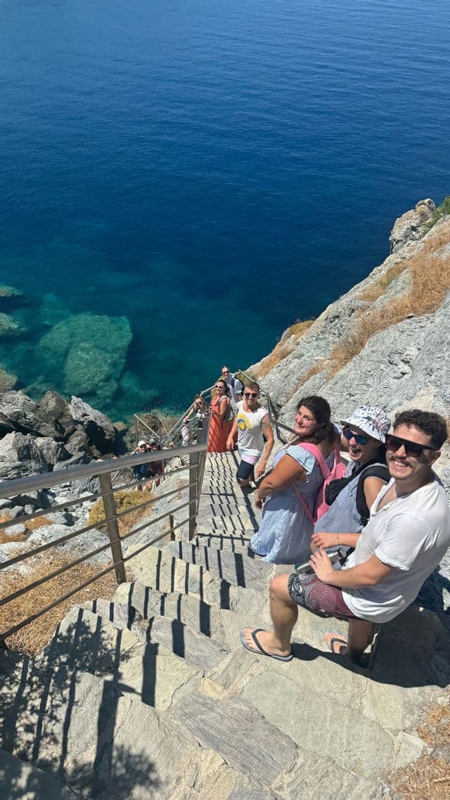 Un gruppo WeRoad sorride salendo una scalinata in pietra costruita nella scogliera che si affaccia sul mare blu.