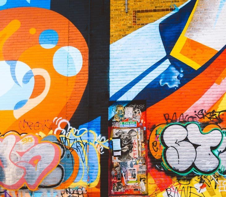 A colorful brick wall covered in various styles of graffiti, with a sticker-covered door in the center.