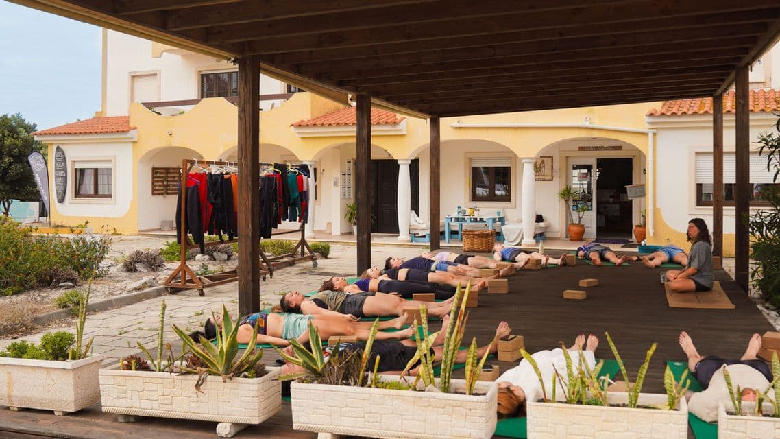 Un gruppo WeRoad si rilassa su tappetini da yoga in posizione Savasana durante una lezione all'aperto su un patio.