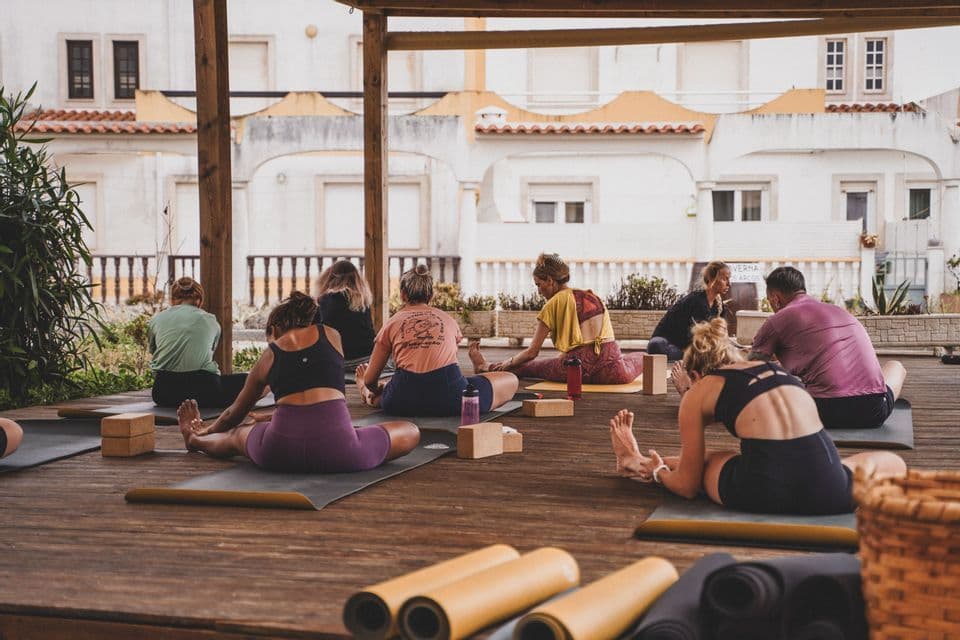 Un gruppo WeRoad in viaggio a una lezione di yoga all'aperto su una pedana di legno, visto da dietro.