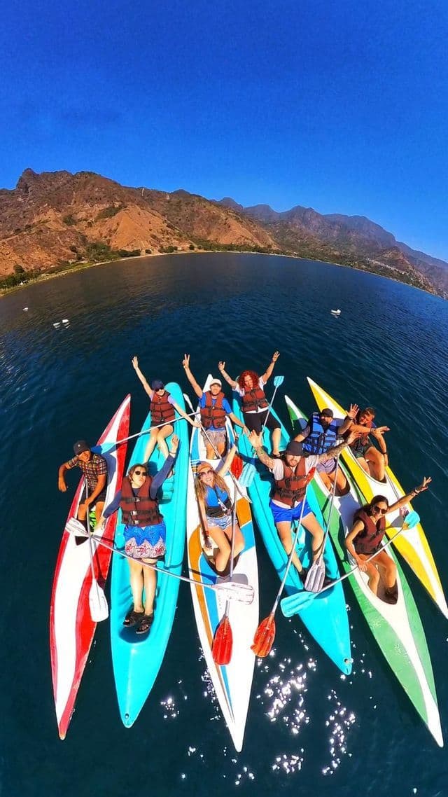 Un grupo de WeRoad saluda desde sus coloridos kayaks en un lago tranquilo, con montañas áridas al fondo.
