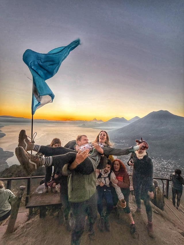 Un viaje en grupo de WeRoad posa para una foto en un mirador de montaña al amanecer, con un lago y montañas de fondo.